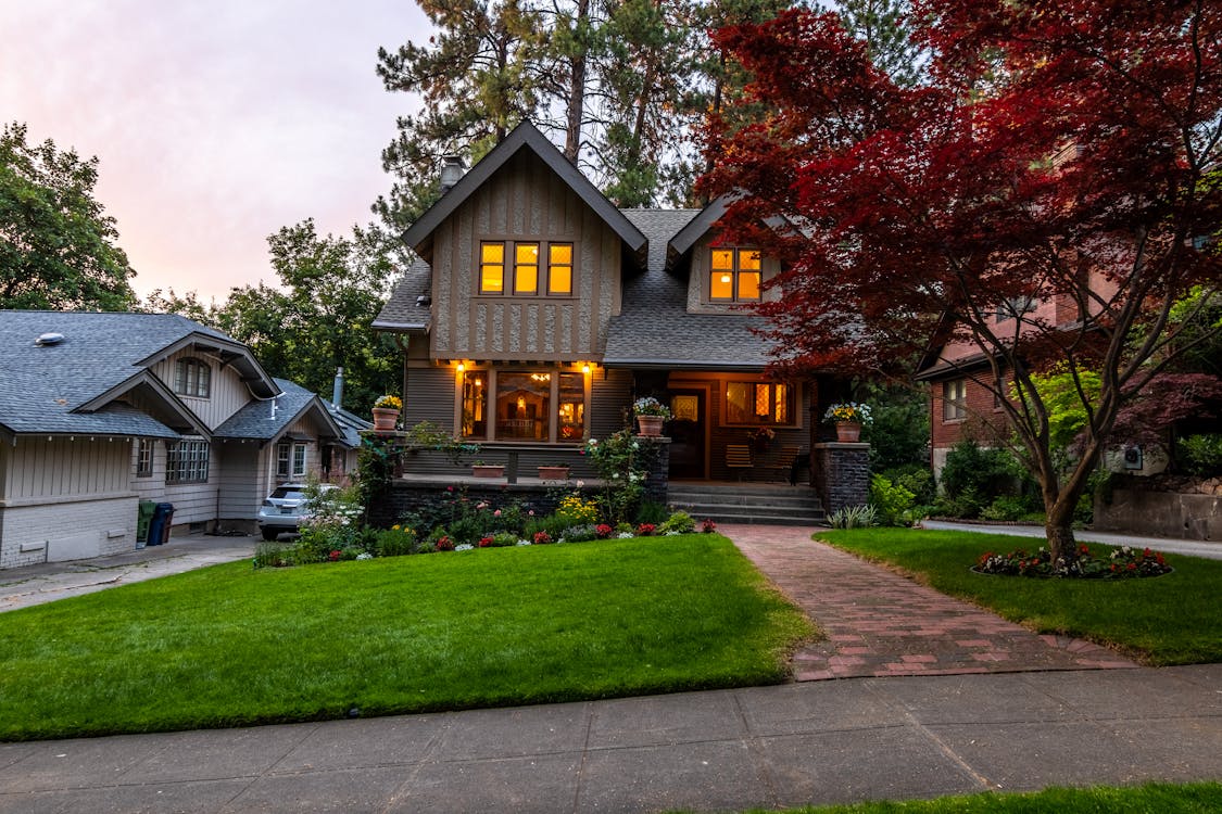 Victorian-style home exterior at twilight with manicured lawn, brick walkway, and lush landscaping
