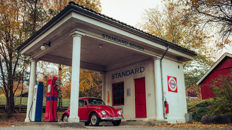 A vintage Standard gas station with red fuel pumps and a classic Volkswagen Beetle