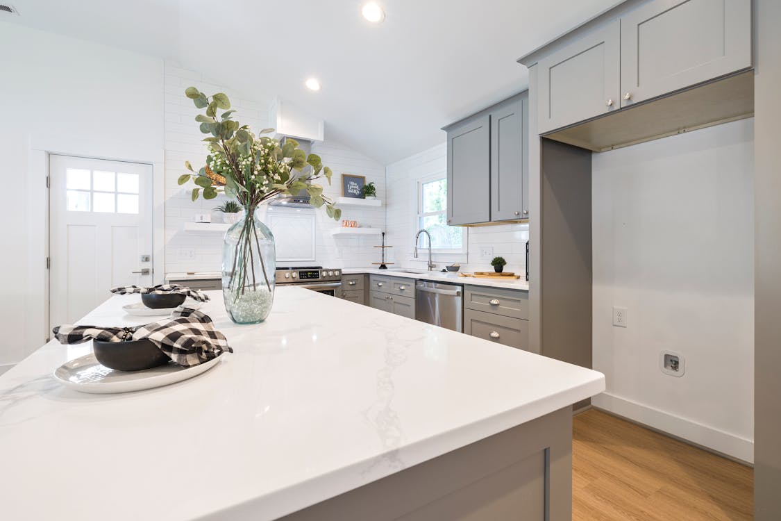 Modern minimalist kitchen with clean white marble countertop, gray cabinets, and a single decorative vase with eucalyptus