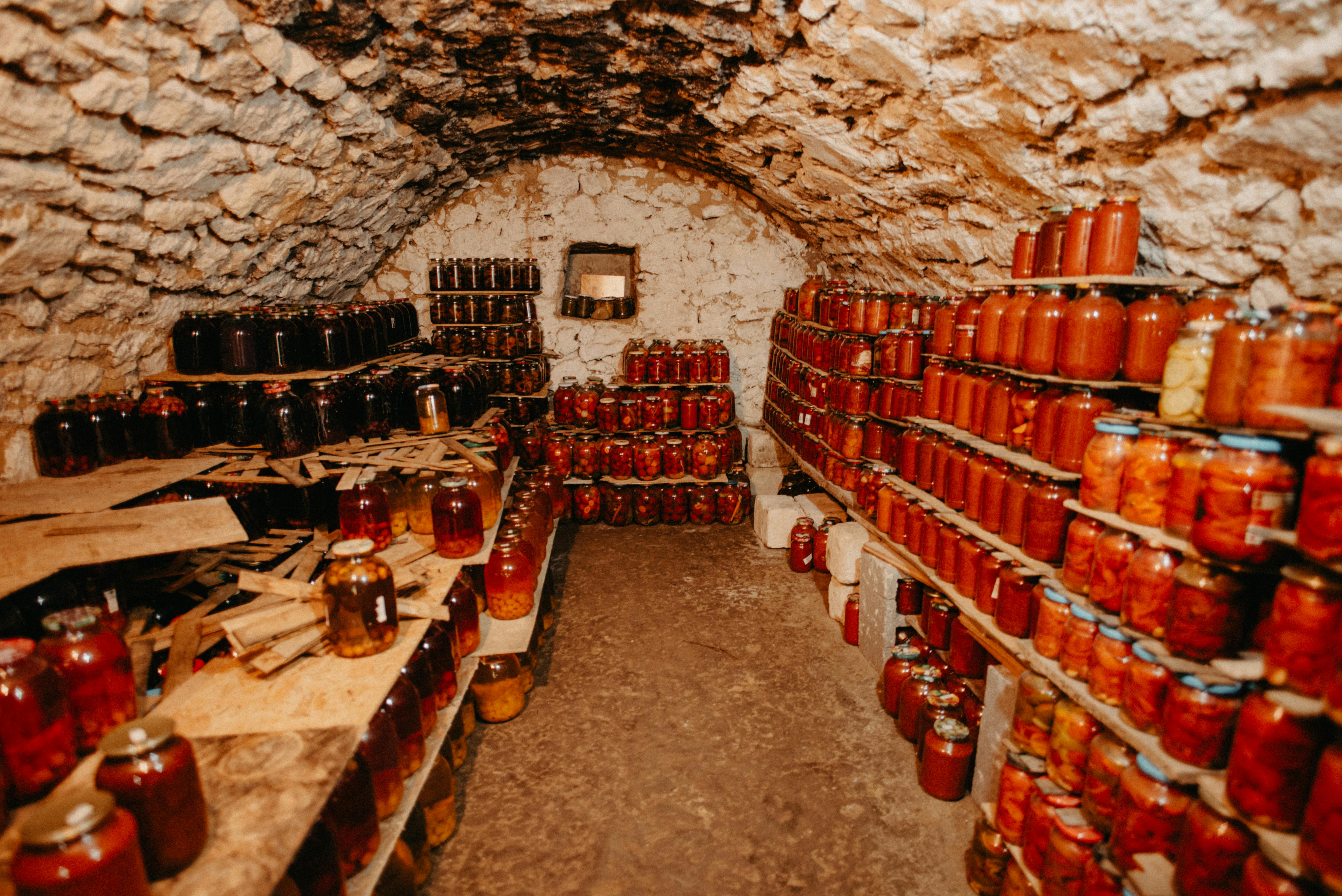 A rustic stone cellar filled with shelves of preserved jars of food