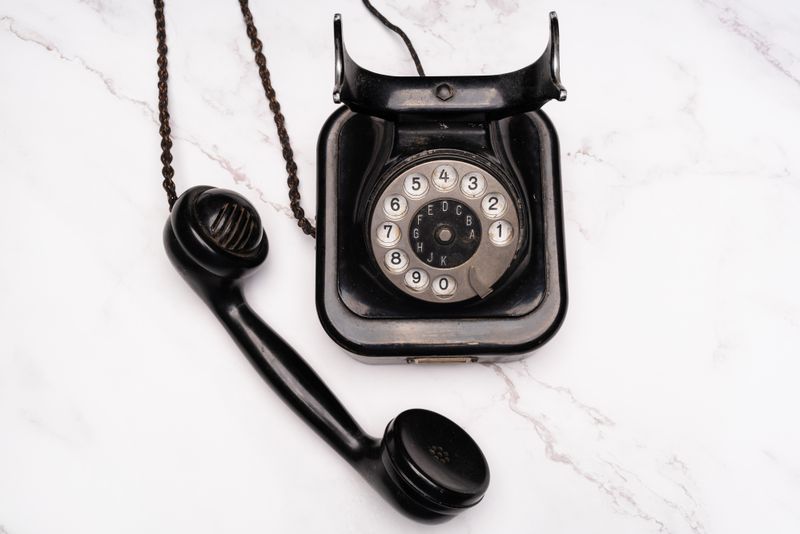 An old-fashioned black rotary dial telephone on a white marble surface